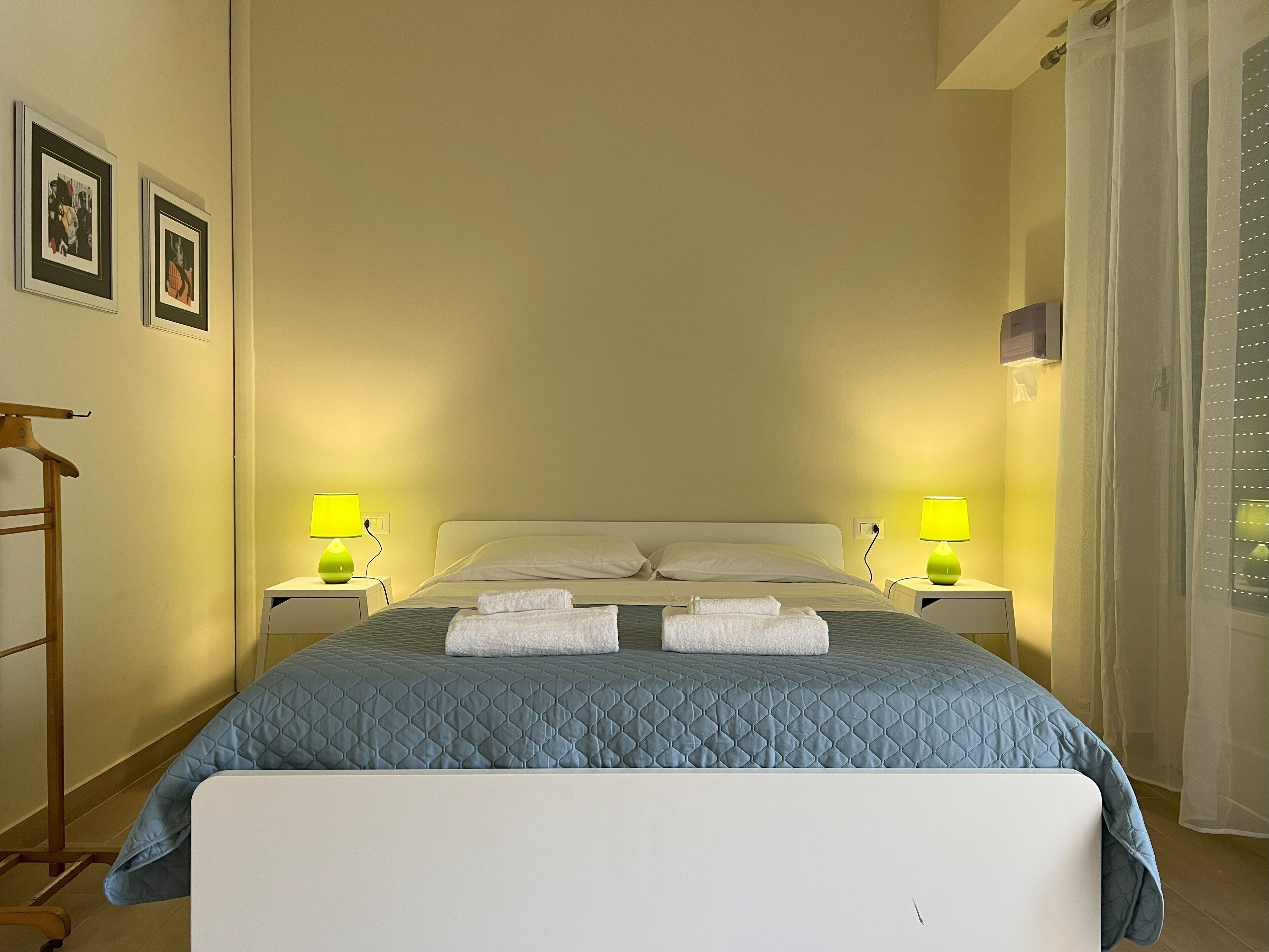 A neatly made bed with a blue quilt, two bedside lamps, and a wooden hanger on the left.