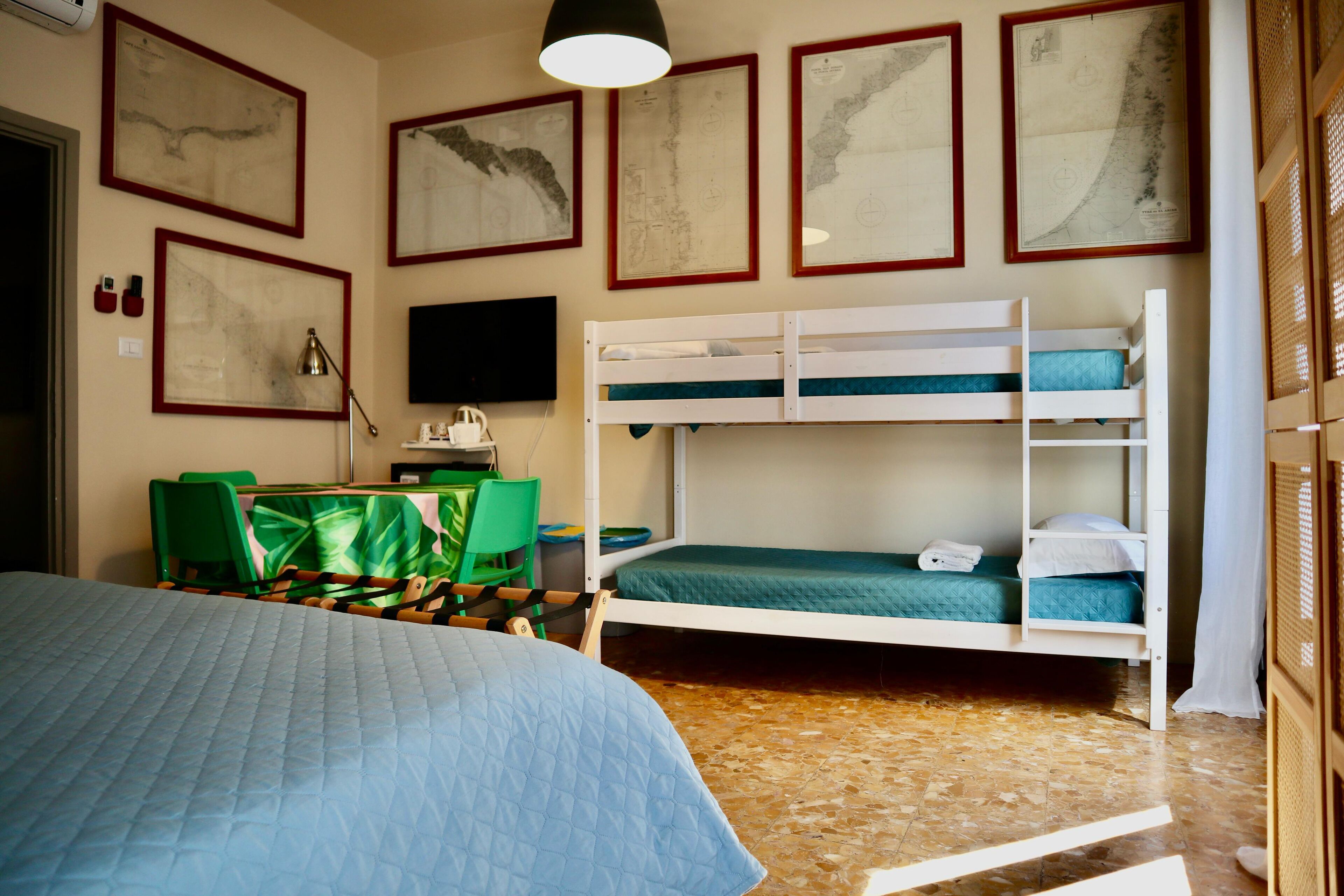 A room with bunk beds, a desk, chairs, and framed maps on the wall.