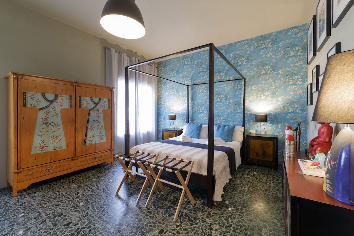 Un dormitorio con una cama con dosel, un armario de madera y piso de baldosas.