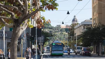 Una scena di strada con un autobus, pedoni e auto parcheggiate.