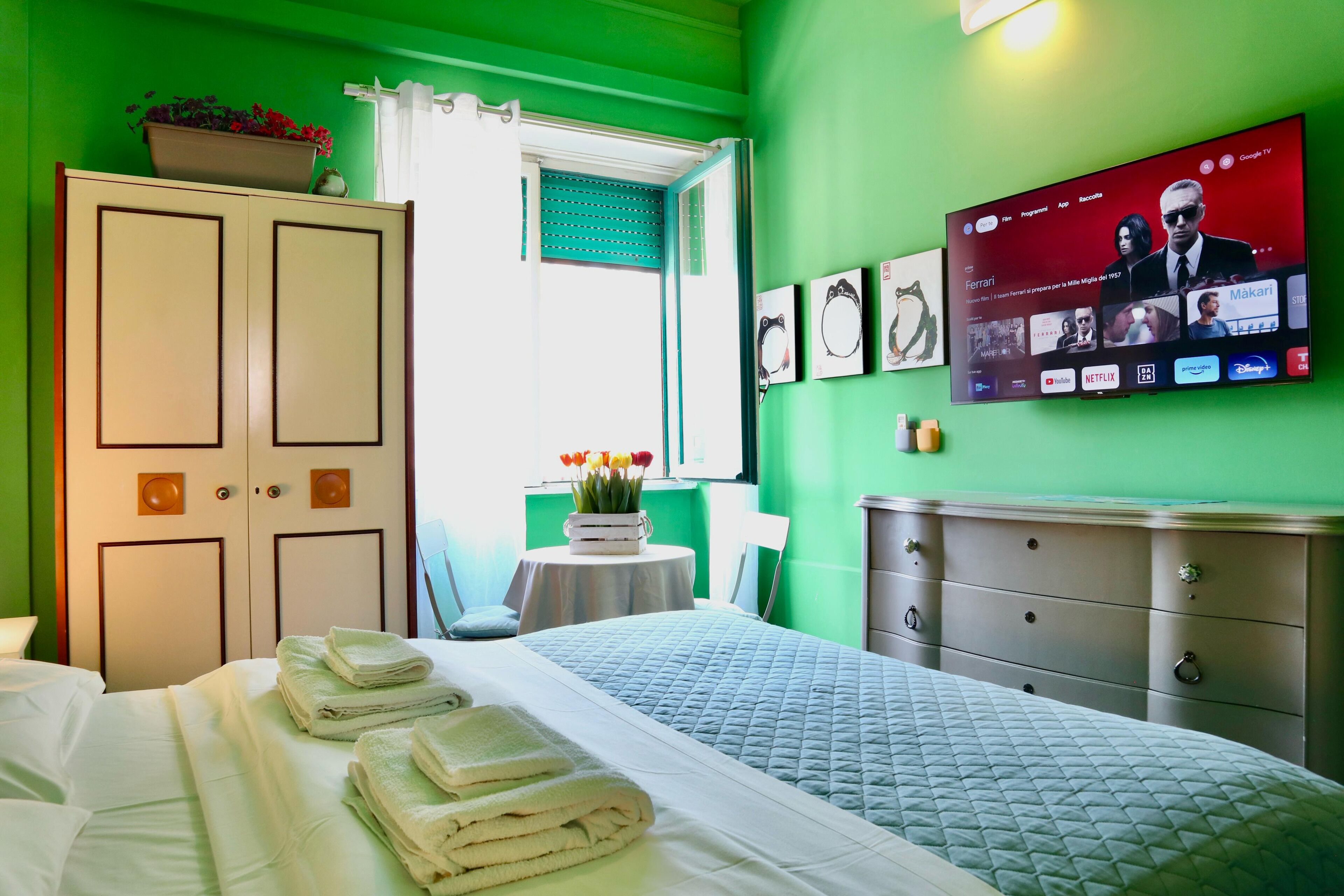 A hotel room with a bed, a wardrobe, a television displaying a movie, and a window with curtains.
