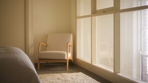 Ein Zimmer mit großem Fenster, einem Sessel und einem Bett.