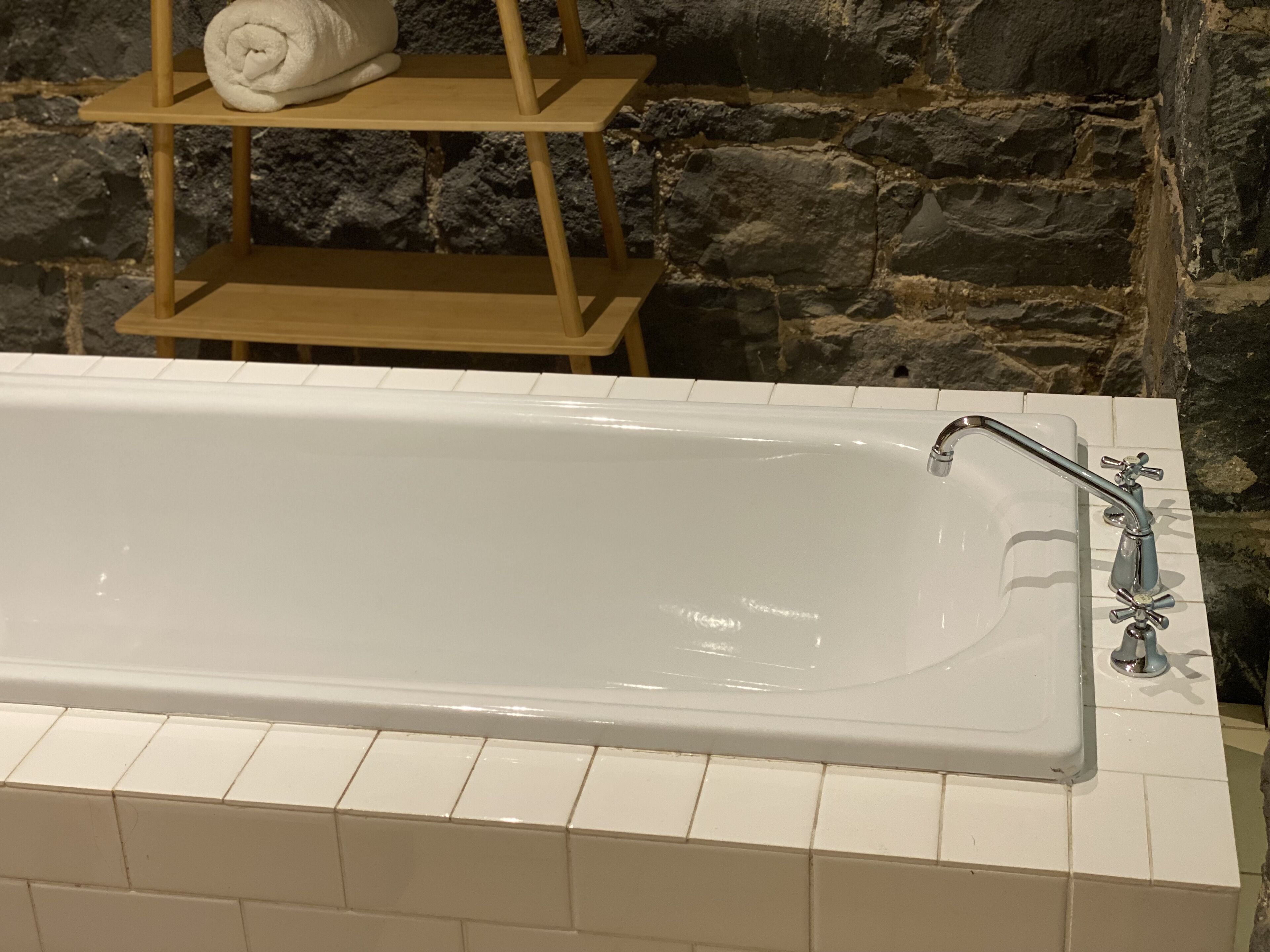 A white bathtub with a modern faucet, set against a stone wall.