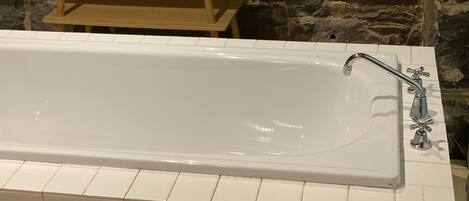 A white bathtub with a modern faucet, set against a stone wall.