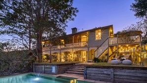 Une maison à deux étages avec une piscine, une terrasse en bois et des guirlandes lumineuses.