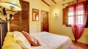 Un dormitorio con cama, lámpara, puerta y ventana con cortinas.