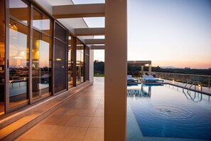 A modern hotel with a glass-enclosed pool area, outdoor seating, and a view of the landscape. - Great sea view villa with heated pool in Agia Marina (Agia Marina, Chania)