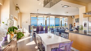 Een moderne keuken met een groot eiland, een eethoek met tafel en stoelen, en uitzicht op de oceaan.