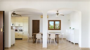 A spacious kitchen with white cabinets, a dining table with chairs, and a ceiling fan.