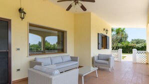 A covered patio area with wicker furniture, a ceiling fan, and a large window.