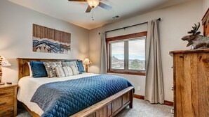 A bedroom with a large bed, a ceiling fan, a window with curtains, and a wooden headboard. - Mountain Lake View - Hot tub/Fireplace! (Estes Park)