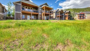 A multi-story residential building with a balcony on the second floor, a covered porch on the first floor, and a grassy yard in front. - Mountain Lake View - Hot tub/Fireplace! (Estes Park)