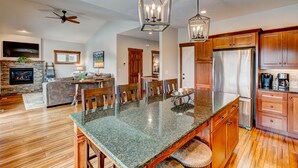 A spacious kitchen with a central island, wooden cabinets, and a stone fireplace. - Mountain Lake View - Hot tub/Fireplace! (Estes Park)