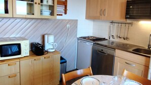 Een compacte keuken met houten kastjes, een magnetron, een koffiezetapparaat, een vaatwasser en een eettafel gedekt voor twee personen.