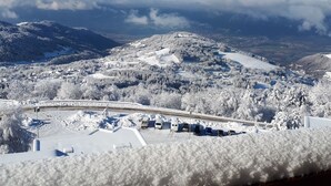 Een besneeuwd landschap met een berg op de achtergrond en een weg met geparkeerde auto's voor.