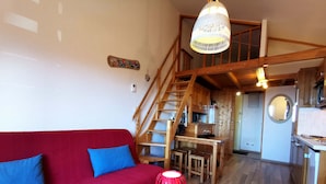 A cozy living room with a red sofa, wooden staircase, and a kitchen area. - Cozy apartment for 4-6 with balcony near slopes, TV, elevator and ski locker (Les Adrets-Prapoutel)