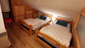 A small, cozy attic bedroom with two wooden beds, a red stool, and a heater. - Cozy apartment for 4-6 with balcony near slopes, TV, elevator and ski locker (Les Adrets-Prapoutel)