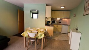 A compact kitchen with a dining area, featuring a table set for four, a microwave, and a refrigerator. - Cozy 2BR Cabin Apartment with Balcony, Near Aquatic Center, Sleeps 6, No Pets (Les Adrets-Prapoutel)