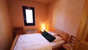 A small, cozy bedroom with a single bed, a nightstand with a lamp, a window, and a wooden door. - Cozy 2BR Cabin Apartment with Balcony, Near Aquatic Center, Sleeps 6, No Pets (Les Adrets-Prapoutel)