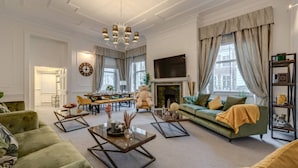 Un salon spacieux avec une cheminée, des canapés verts, une table basse et un coin repas avec des chaises et une table.