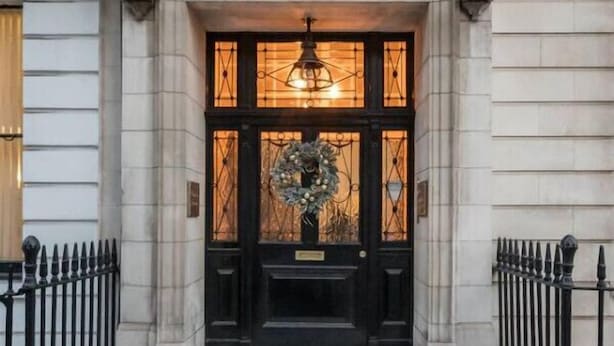Une entrée d’immeuble avec une porte noire, une guirlande et un luminaire au-dessus de la porte.