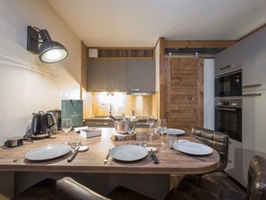 Uma zona de refeições moderna com uma mesa de madeira posta para quatro pessoas, uma máquina de café e uma chaleira.