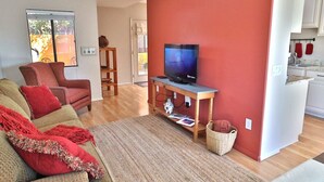 Ein Wohnzimmer mit Fernseher, einer Couch, einer roten Wand und einer Küchenzeile.