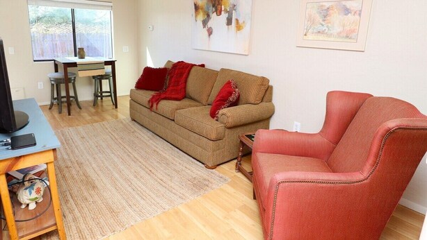 Un salon comprenant un canapé, un fauteuil rouge, une table basse, un téléviseur et une table à manger avec des tabourets.
