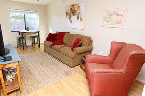 A living room with a sofa, a red armchair, a coffee table, a TV, and a dining table with stools.
