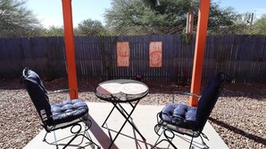 Une terrasse extérieure avec deux chaises et une table, entourée d’une clôture en bois et d’une pergola en métal.