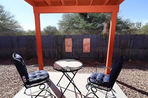 En udendørs patio med to stole og et bord, omgivet af et træhegn og en metalpergola.