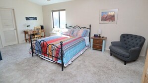 Ein Schlafzimmer mit einem Bett, einem Sessel, einem Nachttisch, einem Schreibtisch, einem Fenster und einem Deckenventilator.