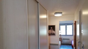 A narrow hallway with a wooden floor, a ceiling light fixture, and a framed picture on the wall.