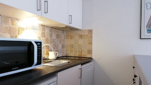 A compact kitchen with white cabinets, a microwave, a Bosch dishwasher, and a tiled backsplash.