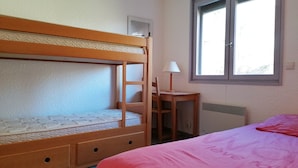A room with a bunk bed, a desk with a chair, a window, and a radiator.