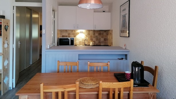 A compact kitchen with a blue island, white cabinets, a microwave, and a hanging pendant light.
