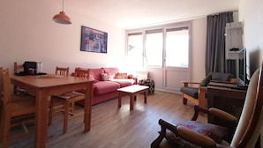 A living room with a wooden dining table, a pink sofa, and a patterned armchair.