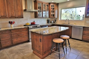 A kitchen with wooden cabinets, a granite countertop, a stove, and a window with birds outside. - The Duke - Iconic Foothills Escape with Pool &Spa (Tucson)