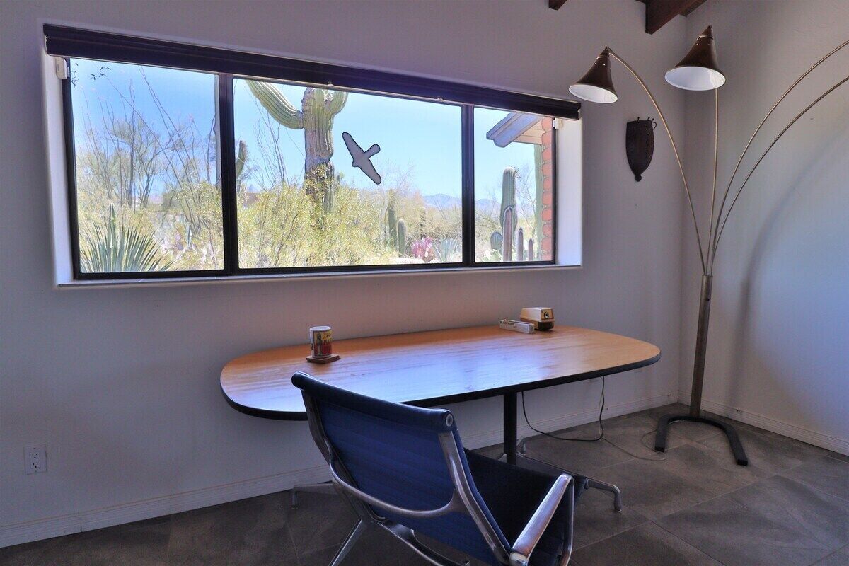 Une pièce avec une grande fenêtre, un bureau, une chaise et deux lampadaires.
