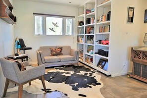 A living room with a sofa, armchair, and a bookshelf filled with books and decorative items. - The Duke - Iconic Foothills Escape with Pool &Spa (Tucson)