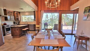 A modern kitchen with a dining area, wooden cabinets, and a large window with a view of palm trees. - The Duke - Iconic Foothills Escape with Pool &Spa (Tucson)