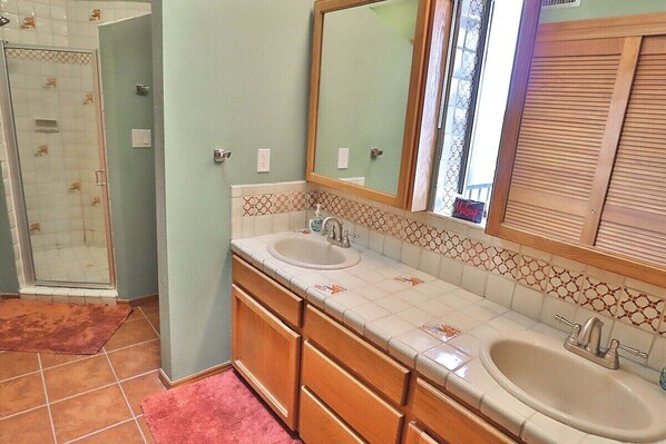Une salle de bain avec une douche, deux lavabos, un miroir et des carreaux décorés.