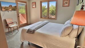 A bedroom with a bed, a chair, a window, and a door. - Desert Paradise at Trails End (Tucson)