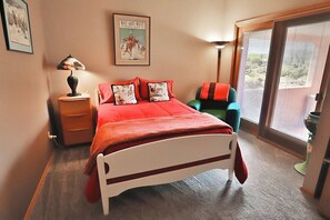 A bedroom with a bed, a nightstand, a lamp, a chair, a window with blinds, and a poster on the wall. - Desert Paradise at Trails End (Tucson)