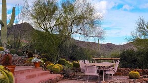 A desert garden with cacti, a wooden table, and chairs. - Desert Paradise at Trails End (Tucson)