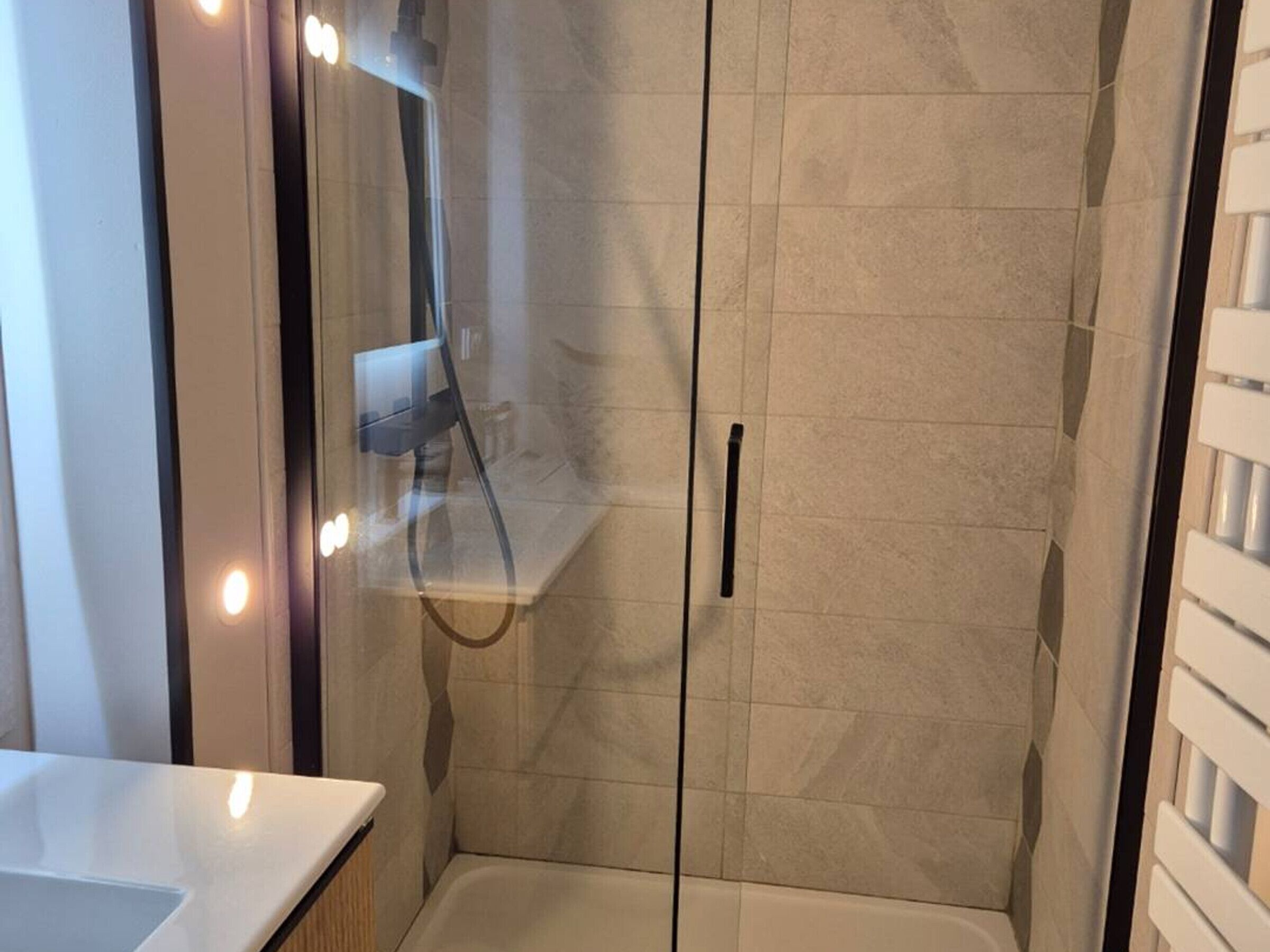Un baño moderno con ducha de vidrio, tocador con espejo y lavamanos blanco.