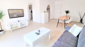 Ein modernes Wohnzimmer mit einem weißen Sofa, einem Couchtisch und einem Essbereich mit einem Holztisch und Stühlen.