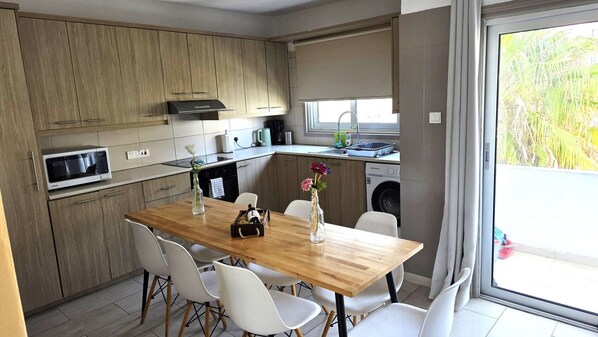 Una cocina moderna con armarios de madera, microondas, lavamanos y comedor con mesa y sillas.