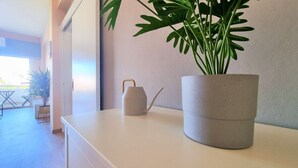 A modern interior with a large potted plant, a white table, and a grey watering can. - The Urban Oasis: Comfort 2br near the City Center! (Larnaca)