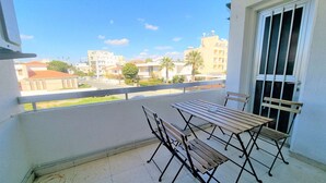 A balcony with a table and chairs, overlooking a residential area with buildings and trees. - The Urban Oasis: Comfort 2br near the City Center! (Larnaca)